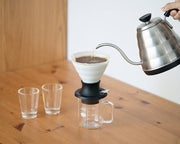 HARIO USA - HARIO Ceramic Immersion Dripper 02 SWITCH in use with a gooseneck kettle, showcasing a precise pour-over coffee setup on a wooden table.