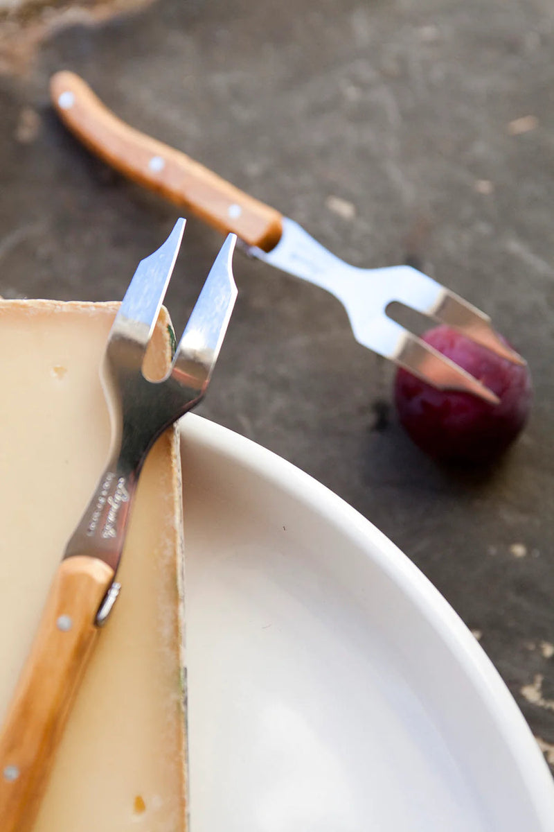 Be Home | Mini Cheese Fork - Olivewood, elegantly crafted silverware piece, ideal for cheese platters, showcased on a plate with a spoon and knife.