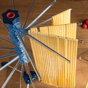 Marcato | Tacapasta Pasta Drying Rack, Red, on wooden countertop, holds fresh pasta noodles draped over stainless-steel rods, showcasing its efficient drying capability for homemade pasta.