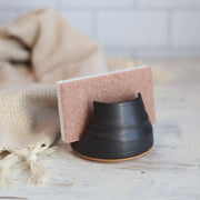 Gravesco Pottery - Sponge Holder in Black, showcasing a matte-black ceramic holder with a pink-and-white sponge, complemented by a cream kitchen cloth on a wooden surface.