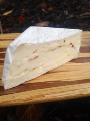 Tulip Tree Creamery - Snapdragon: A wedge of triple cream bloomy rind cheese with habanero peppers, showcasing its creamy interior on a wooden cutting board.