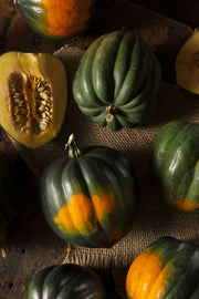 Bentley Seed Co. - Squash-Acorn Table Queen 1913, featuring whole and halved acorn squash on a wooden surface, highlighting its ribbed skin and pale orange flesh.