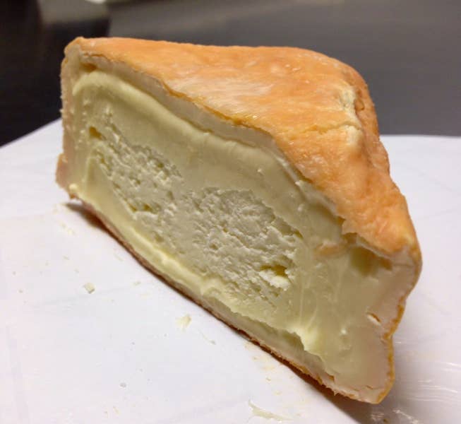 Tulip Tree Creamery - Foxglove cheese slice on a white surface, showcasing its soft, runny texture, highlighting its culinary appeal from Athens Cooks.