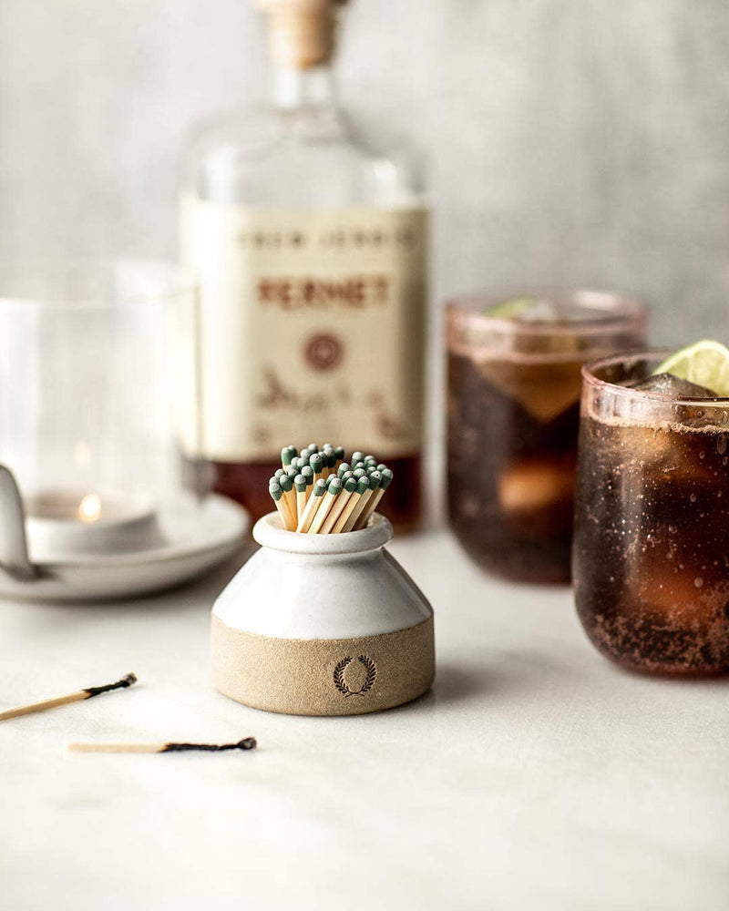 Farmhouse Pottery - Milk Bottle Match Striker with muted green matches, a lit tealight, and fernet cocktails, showcasing elegant match lighting for candles.