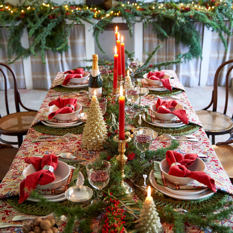 Couleur Nature - Noel Red & Green tablecloth adorns a festive dining setup with woven chargers, crystal goblets, and pine garland, embodying casual holiday elegance.