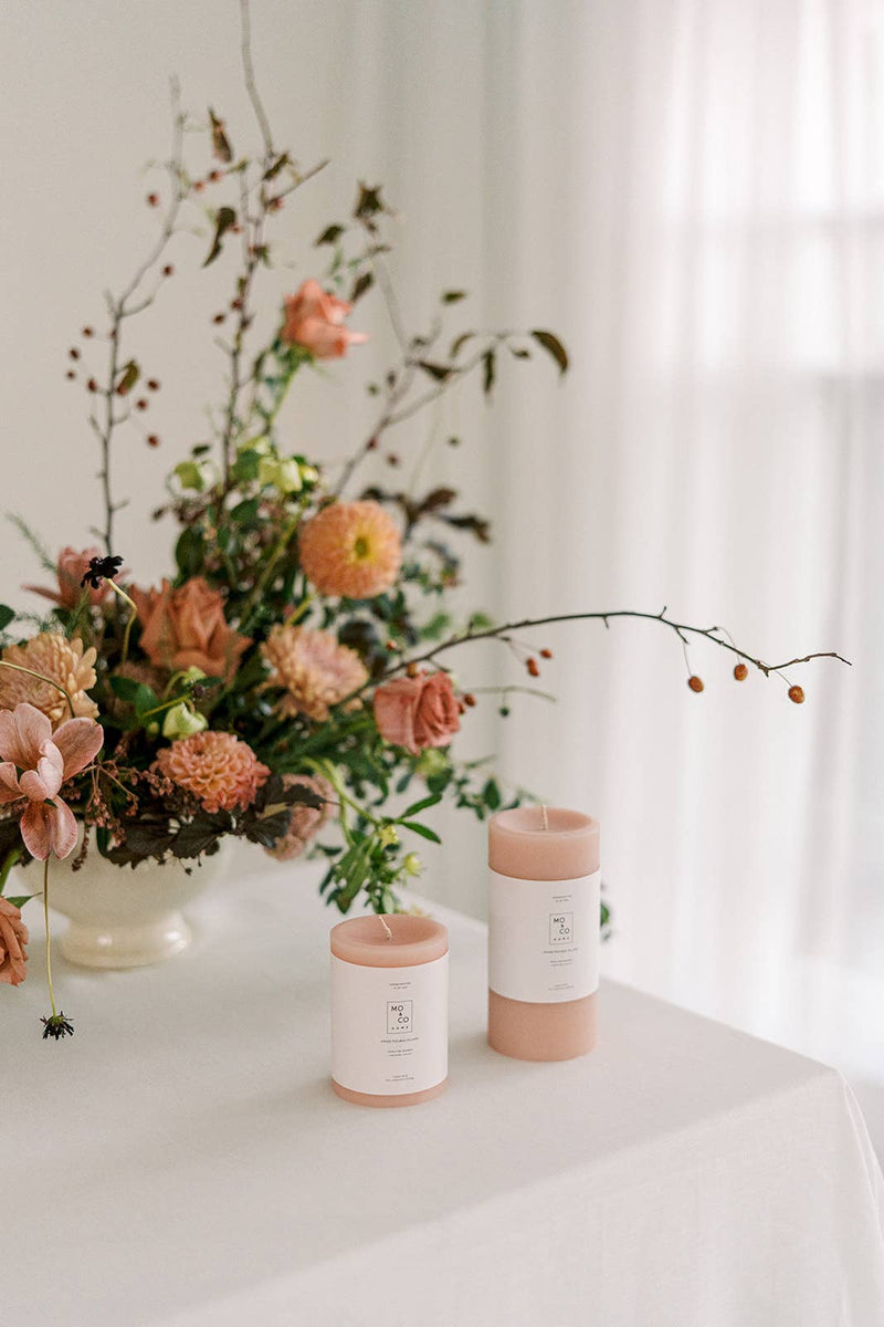 Mo&Co Home - 100% Beeswax Pillar Candles | Rose Pink: 3x4 Inch, surrounded by flowers, displayed on a table, ideal for home decor and special occasions.