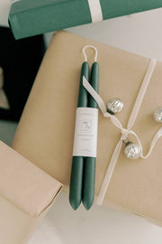 Mo&Co Home - Forest Green Dipped Beeswax Taper Candles styled on gift boxes with ribbons, reflecting a holiday aesthetic; made from 100% beeswax, supporting eco-conscious practices.