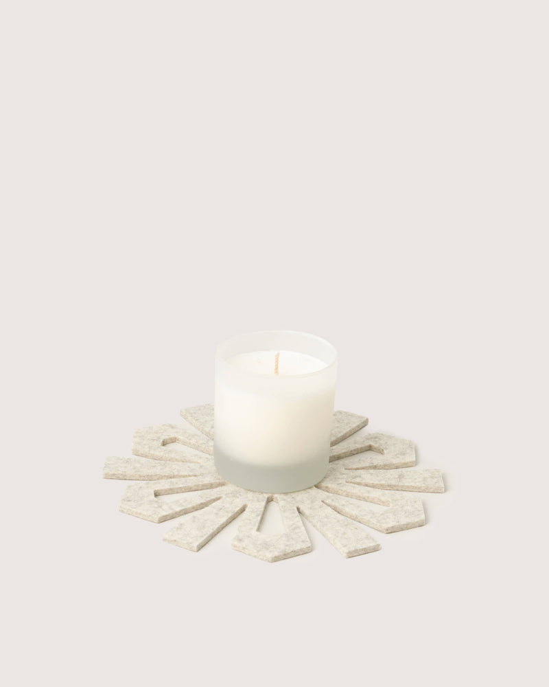 Graf Lantz - Merino Wool Snowflake Trivet in Heather White with a white candle in frosted glass, showcasing its unique design and practicality for holiday decor.