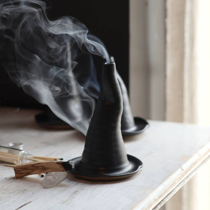 Gravesco Pottery - Witch Hat Incense Burner: Two black, conical burners with smoke rising, matching saucers, surrounded by a palo santo stick, matchsticks, and quartz crystal.