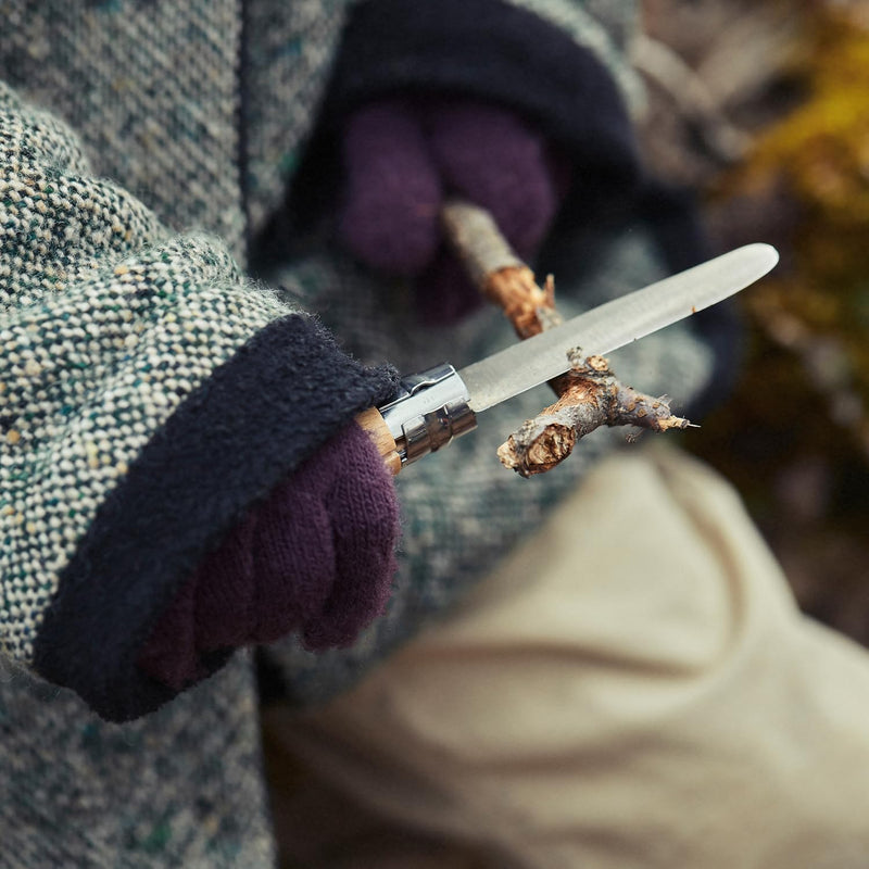 Person outdoors whittling a branch with the Opinel | N°7 First Opinel Folding Knife, featuring a safe round-ended blade and Virobloc locking ring.