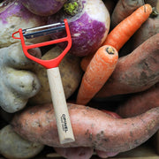 Opinel | T Duo Peeler with Wooden Handle, Red, shown atop root vegetables, featuring dual stainless steel blades for peeling and julienning, ideal for versatile kitchen tasks.