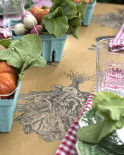 Hester & Cook | Farmer's Market Runner displayed on a table with various fresh vegetables and a glass, highlighting its use for elegant kitchen and dining setups.