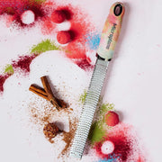 Microplane | Premium Zester, Grater - Ombre surrounded by cinnamon sticks, ground cinnamon, colorful powders, and confectionery balls, highlighting its versatile culinary use.