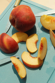 The MK Free Board, Ocean, showcases a sliced peach and knife, highlighting its non-porous, plant-based surface, ideal for safe, eco-friendly kitchen use.