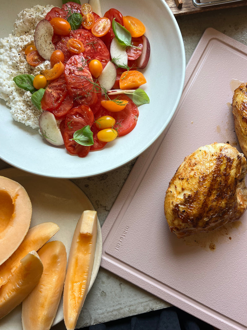 The MK Free Board, Ocean, showcasing its eco-friendly design, supports a summertime meal prep with roasted chicken and tomato salad, emphasizing safe and efficient kitchen use.