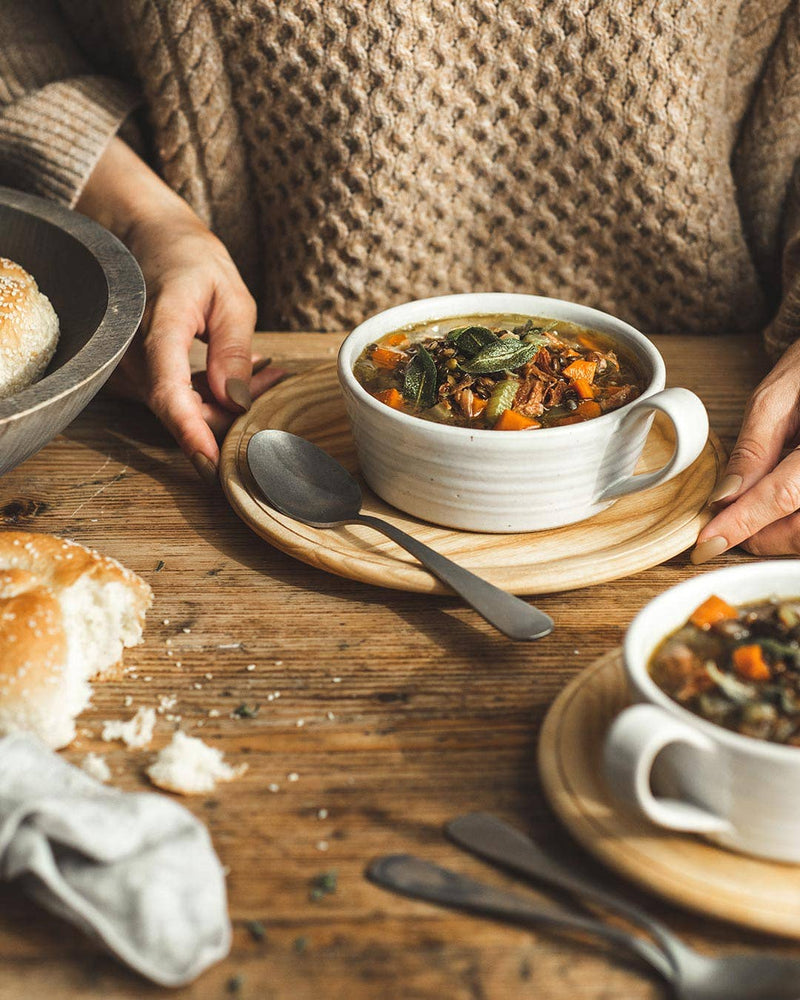 Farmhouse Pottery - Silo Soup Mug filled with hearty vegetable broth on a wooden plate, accompanied by sesame bread, showcasing its rustic design and versatile use.