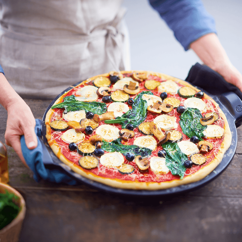 Emile Henry | Smooth Pizza Stone, Charcoal: A freshly baked vegetable pizza on the stone, highlighting its ability to achieve a golden, crispy crust like a traditional pizza oven.