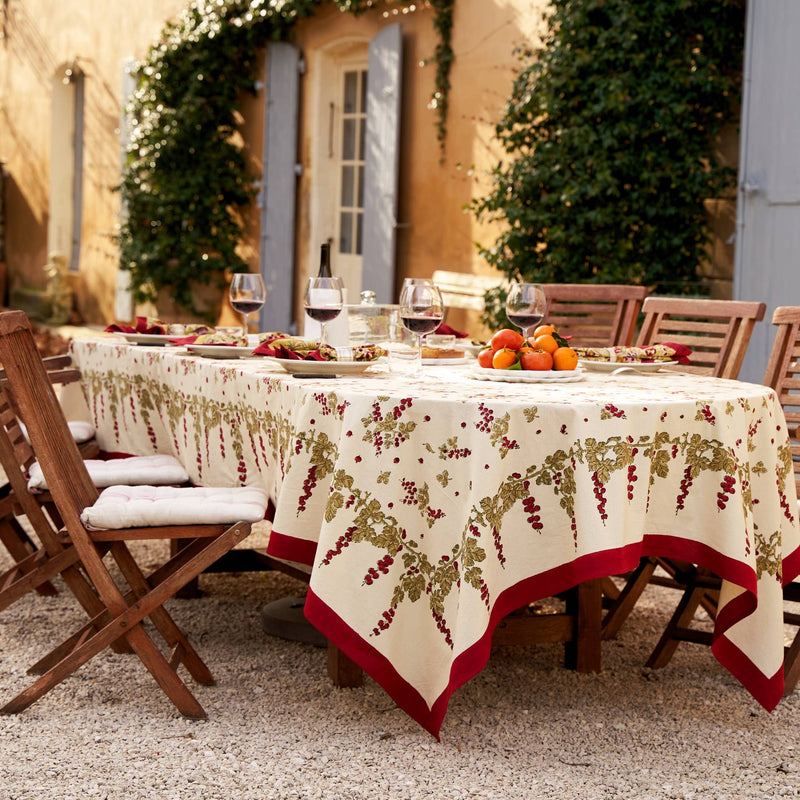 Couleur Nature - Gooseberry Red & Green French Tablecloth, 59x86, drapes a sunlit outdoor table with grapevine patterns, enhancing an elegant courtyard dining scene.