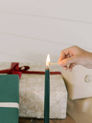 Hand lighting a Mo&Co Home - Forest Green Dipped Beeswax Taper Candle, 14 Inch, perfect for elegant home decor and eco-friendly celebrations.