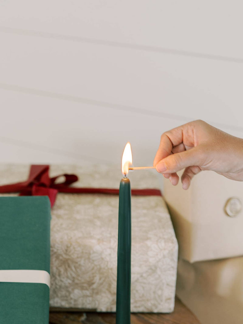 Hand lighting a Mo&Co Home - Forest Green Dipped Beeswax Taper Candle, 14 Inch, perfect for elegant home decor and eco-friendly celebrations.