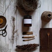 Among the Flowers - Essential oil candle | HOLIDAY: Hearth, centered in a rustic flat-lay with natural elements like a pinecone, twig, and vintage book.