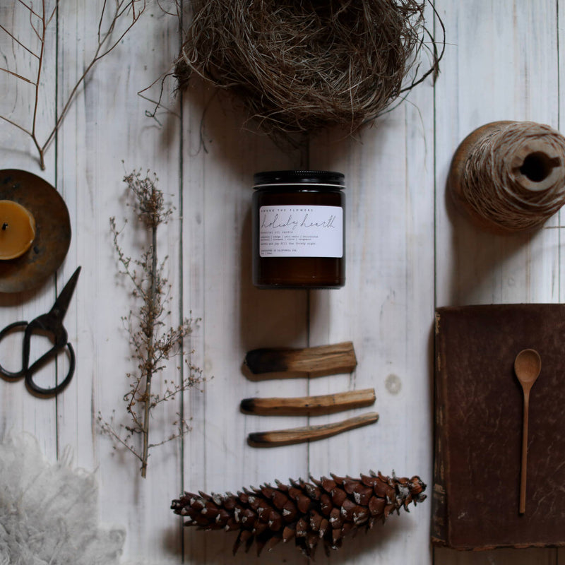 Among the Flowers - Essential oil candle | HOLIDAY: Hearth, centered in a rustic flat-lay with natural elements like a pinecone, twig, and vintage book.