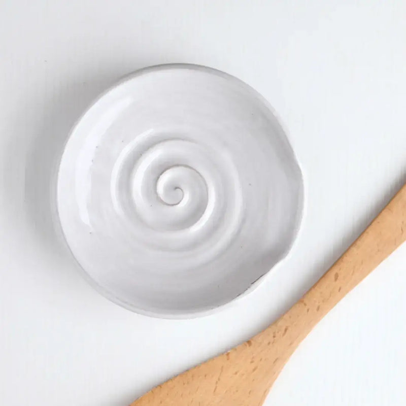 Gravesco Pottery handmade spoon rest with spiral design, paired with a wooden utensil, ideal for keeping stovetop areas clean.