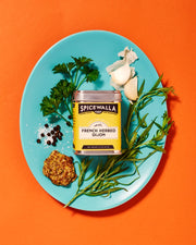 Spicewalla | French Herbed Dijon jar on a blue plate, featuring herbs and spices like tarragon, mustard, garlic, and white pepper.