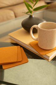 Graf Lantz - Bierfilzl Merino Wool Felt Square Coaster Solid 4 Pack: Turmeric on a table with a white mug and plant vase nearby.