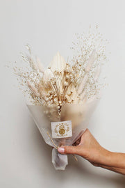Idlewild Floral Co. - Snow Dried Flower Bouquet: A hand-tied bundle of bleached baby's breath and bunny-tail grass, elegantly wrapped with a label, held against a neutral background.