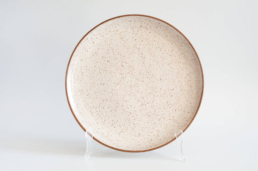 RachaelPots - Serving Platter: Sage, a round, speckled ceramic plate with a brown rim, displayed upright, showcasing its handcrafted elegance for enhancing dinner presentations.
