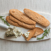 Potters Table - Salted Olive Oil Flatbreads on a marble board with herbed goat cheese, rosemary, and a cheese knife, highlighting their rustic, crunchy texture.