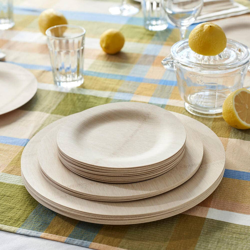 bambu® Disposable Bamboo Round Plates: 11 inches, neatly stacked on a checkered tablecloth, surrounded by lemons and a citrus juicer, showcasing an eco-friendly dining option.