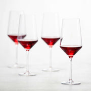 Zwiesel Fortessa | Pure Bordeaux Glass, 23oz: Four Tritan Crystal wine glasses, with elegant stems and angled bowls, partially filled with red wine, enhancing sophisticated sipping experiences.