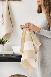 Woman holding MagicLinen striped linen tea towel, showcasing its texture and loop for hanging, highlighting the zero-waste design and practicality for kitchen use.