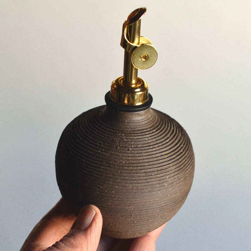 Hand holding Rose Line Pottery Oil Bottle, a handcrafted, ribbed-clay vessel with brass pump, ideal for olive oil, vinegar, or syrups.