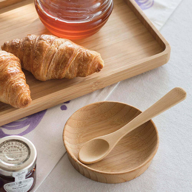 Bamboo tea spoon on a tray with croissants and honey, illustrating its eco-friendly, versatile use for stirring or serving, available at Athens Cooks.