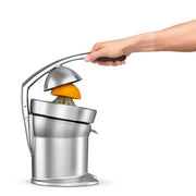 Breville | Citrus Press Pro in action, squeezing an orange with a lever-style design, featuring a finned juicing cone for maximum extraction, collecting juice in a container with spout.