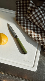 Material - The MK Free Board: Cloud, featuring a paring knife, potato, and checkered cloth, showcased on a stainless-steel surface for efficient, eco-friendly kitchen prep.