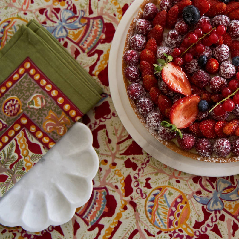 Berry tart on a white plate, set on a Couleur Nature - Noel Red & Green French tablecloth with festive, handprinted holiday patterns, alongside olive napkins.
