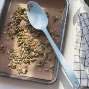 GIR | Ultimate Spoon - Studio White on a tray with seeds, showcasing its versatile deep bowl and flexible edges for efficient kitchen use.