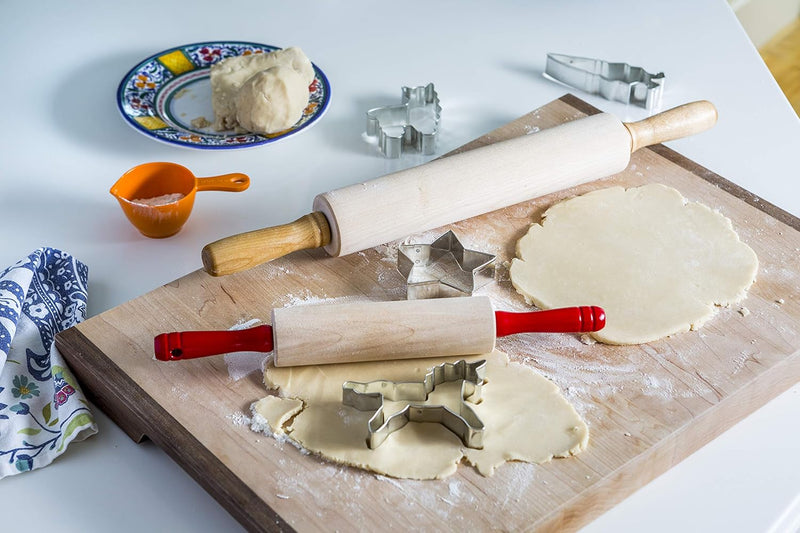 Kid's rolling pin with red handles on a cookie-making setup, featuring rolled dough, metal cookie cutters, and a measuring cup. Perfect for young bakers at Athens Cooks.