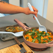 GIR | Ultimate Spoon - Studio White: A person uses the versatile kitchen tool to stir food in a pan, highlighting its deep bowl and flexible edges.