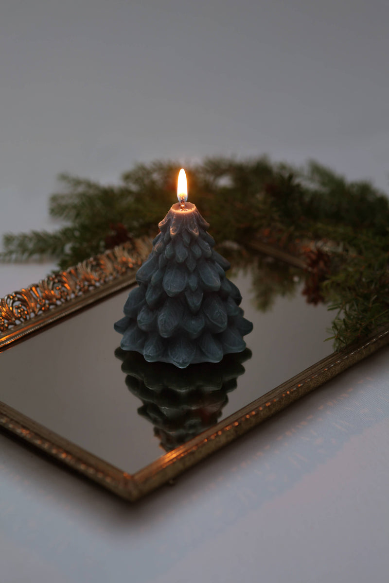 Mo&Co Home Exclusive: Sculpted Beeswax Tree candle on mirror, reflecting its intricate evergreen design, surrounded by real boughs; embodies holiday nostalgia and elegance.
