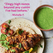 Skewered grilled chicken with herb sauce on flatbread, highlighting Diaspora Spices Co. - Jodhana Cumin's unique flavor. Accompanied by tomatoes, peppers, and extra sauce.