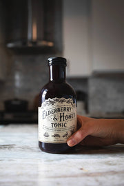 Roots And Leaves - Elderberry & Honey Tonic, 16 oz bottle, held in hand, showcasing label featuring herbal blend for immune support.