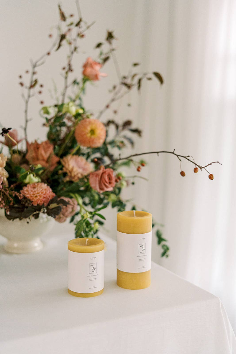 Mo&Co Home - 100% Beeswax Pillar Candles | Natural Gold: 3x6 Inch, two candles on a table, highlighting sustainable, hand-poured craftsmanship.