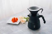 HARIO USA - V60 Metal Dripper: Silver showcased on a minimalist tabletop with a black coffee server, strawberries, and roses, highlighting precision brewing elegance.