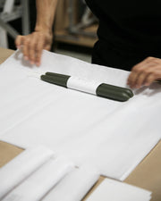 Mo&Co Home - Forest Green Dipped Beeswax Taper Candles, handcrafted, 14-inch, lie wrapped on white paper, hands folding for eco-friendly packaging.