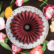 Nordic Ware | Brilliance Bundt® Pan featuring a red bundt cake on a plate, surrounded by flowers, showcasing its elegant design and nonstick surface.